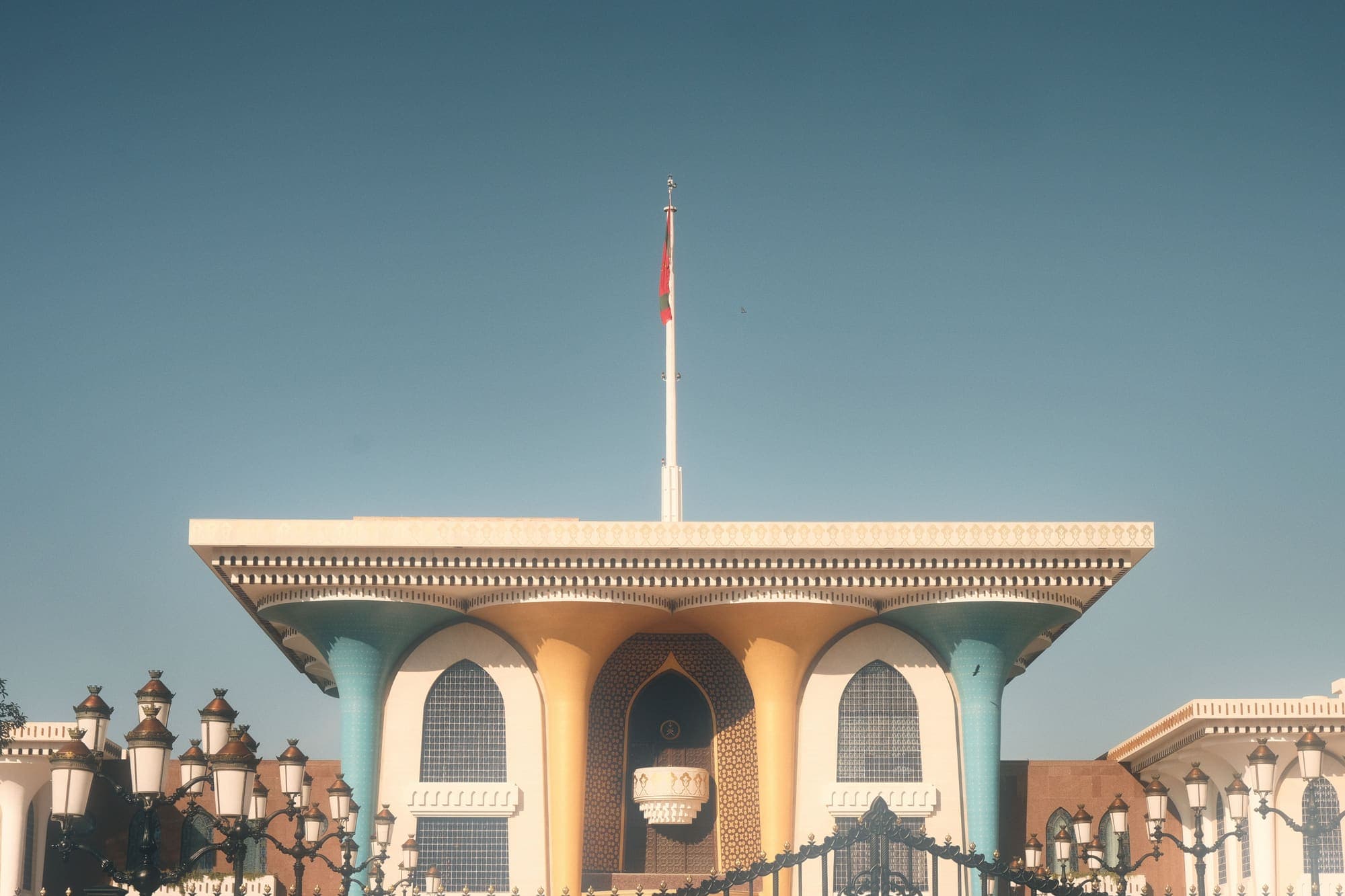 A fachada do Palácio Al Alam, em Mascate, com colunas azuis e douradas e a bandeira de Omã no alto.