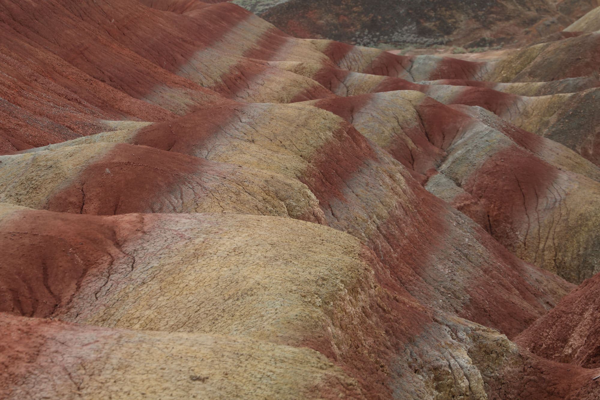 Faixas de vermelho e creme atravessando as encostas arredondadas das montanhas coloridas de Zhangye.