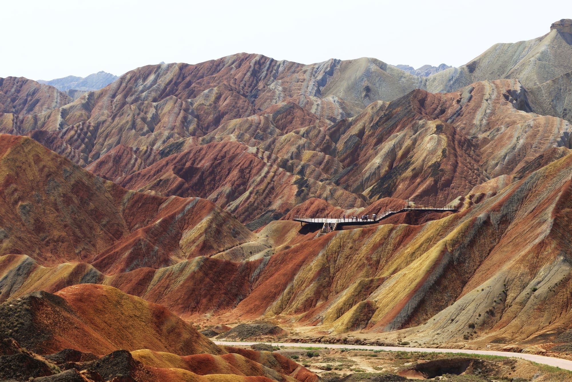 Um vale das montanhas coloridas de Zhangye, com encostas em faixas de várias cores e uma estrada ao fundo.