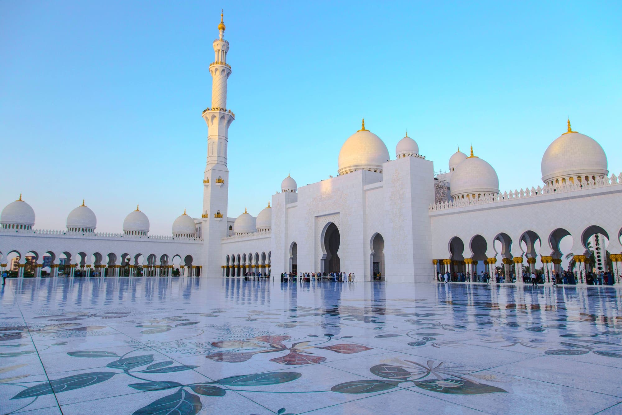 O pátio de mármore branco com desenhos de flores da Grande Mesquita Sheikh Zayed, em Abu Dhabi, com as cúpulas e um minarete.