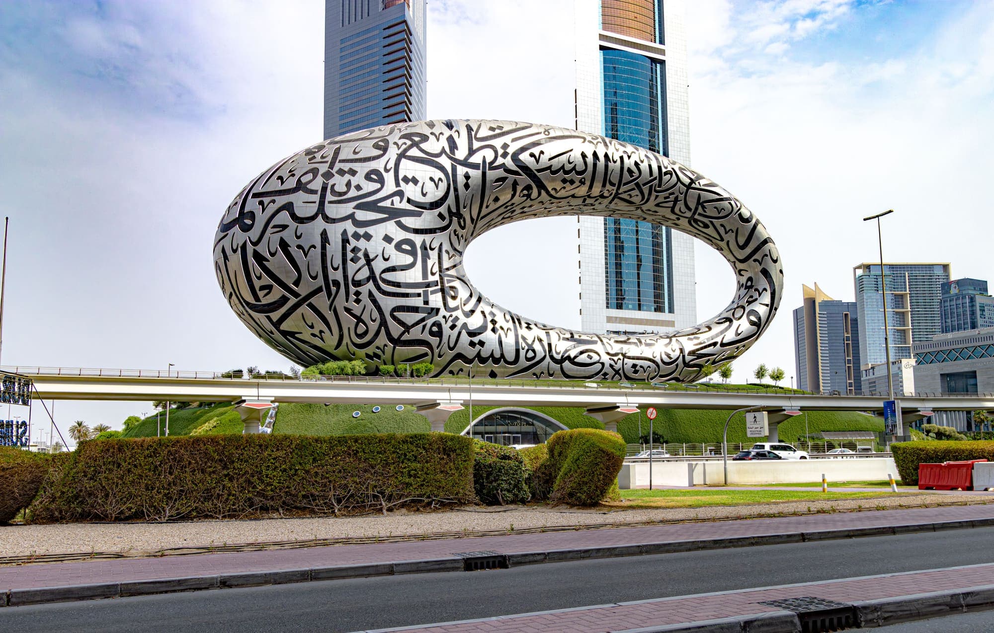 O Museu do Futuro, em Dubai: um anel de aço inoxidável com a fachada recortada em caligrafia árabe, sobre um morro gramado.