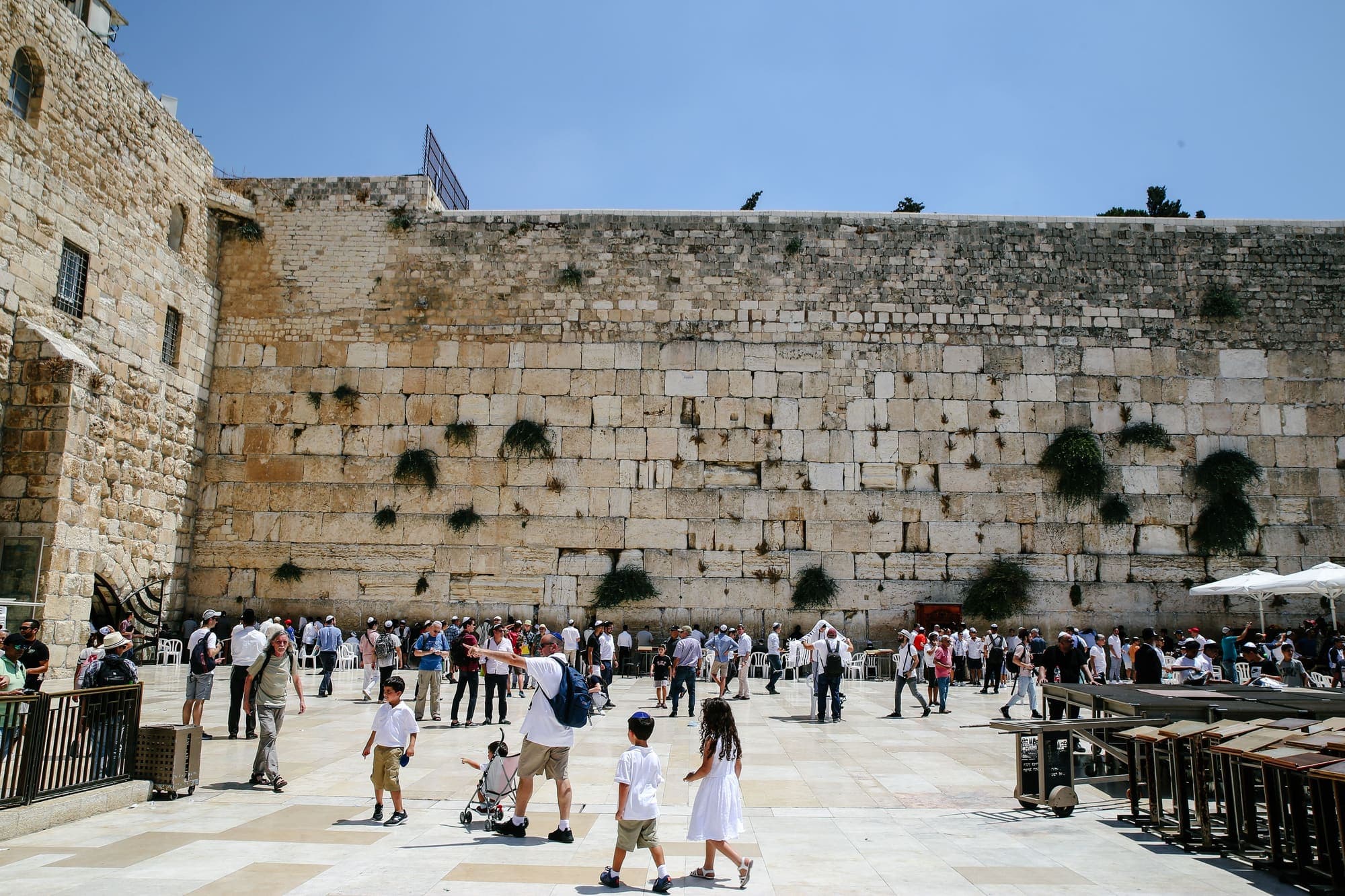 A praça do Muro das Lamentações, em Jerusalém, com visitantes diante do muro de grandes blocos de pedra.