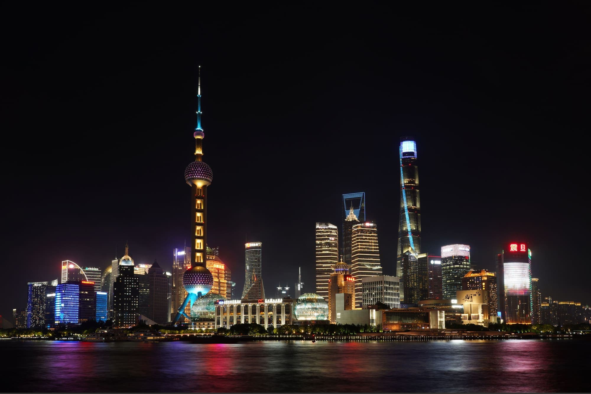 Os arranha-céus de Pudong iluminados à noite e refletidos no Rio Huangpu, em Xangai.