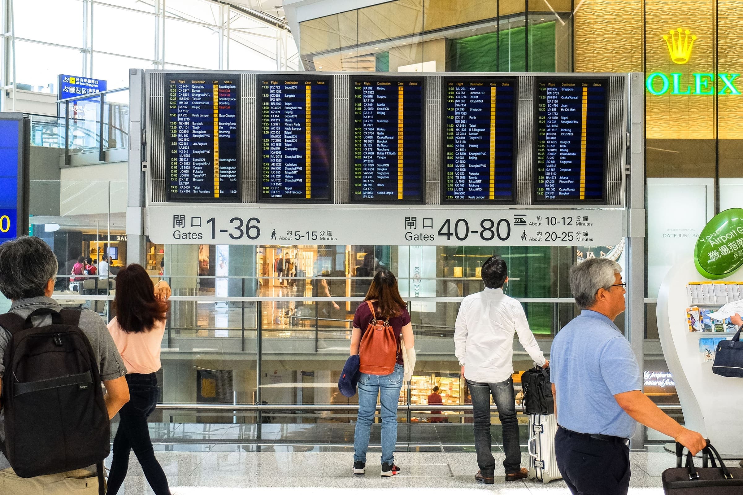 Viajantes diante do painel de partidas de um aeroporto, conferindo voos e portões de embarque.
