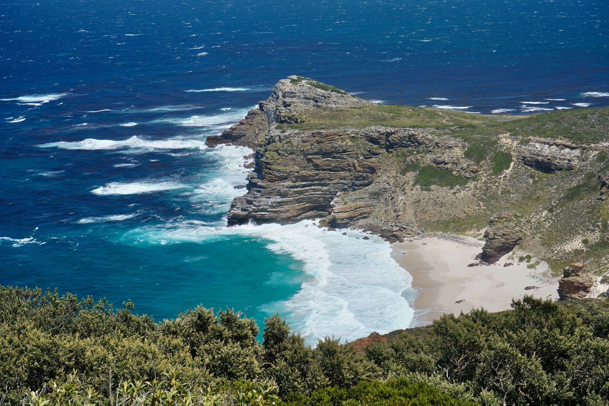 O promontório do Cabo da Boa Esperança e a pequena praia de Dias Beach, vistos de Cape Point, com o mar azul do Atlântico.