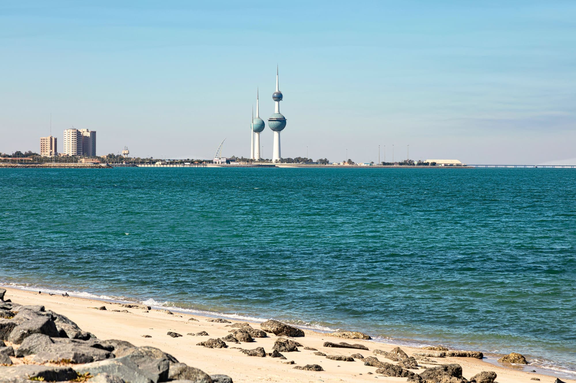 As Torres do Kuwait vistas de uma praia de Kuwait City, do outro lado do mar azul-turquesa.