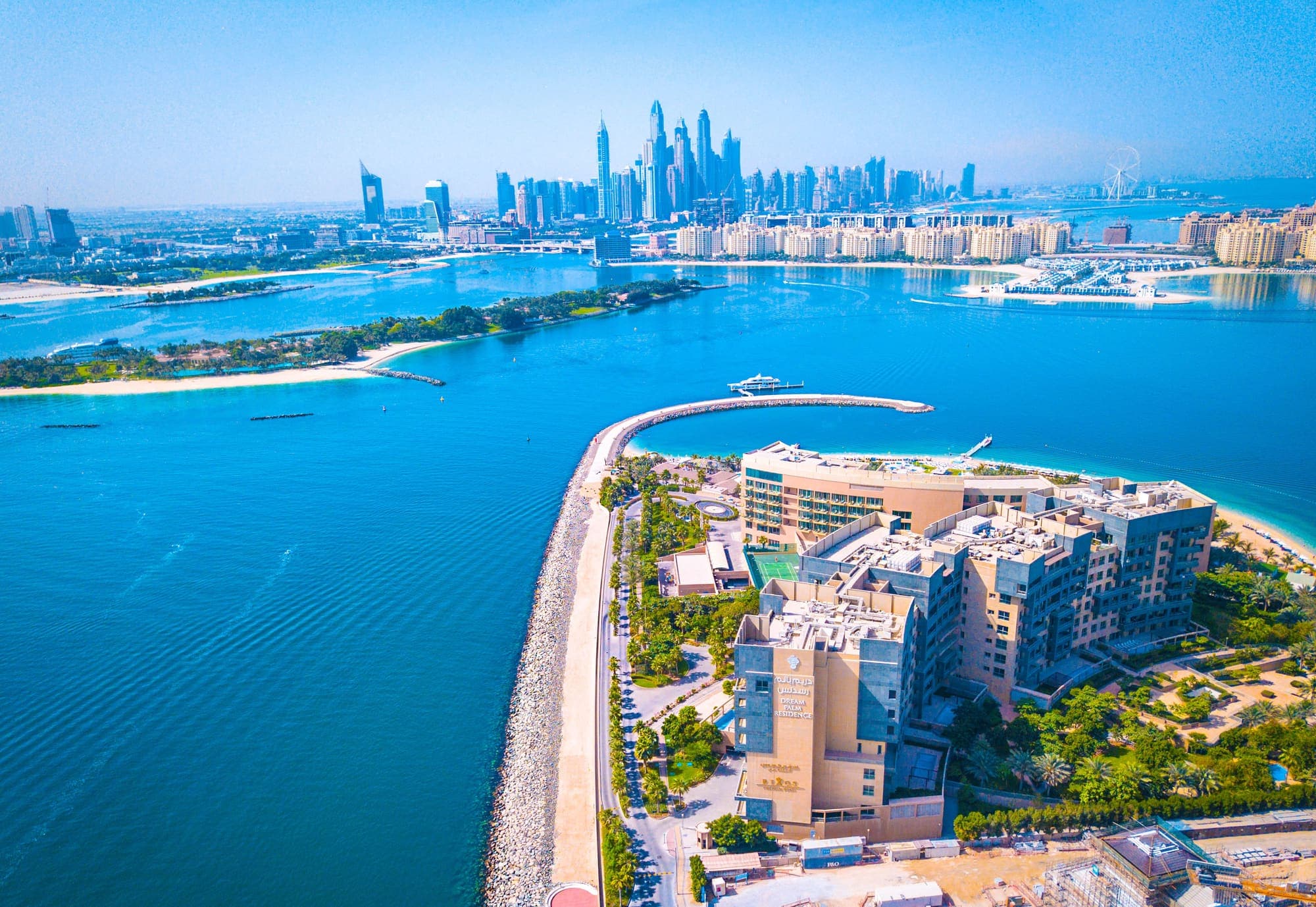 Vista aérea de Dubai, com o mar azul em primeiro plano e os arranha-céus da Marina ao fundo.