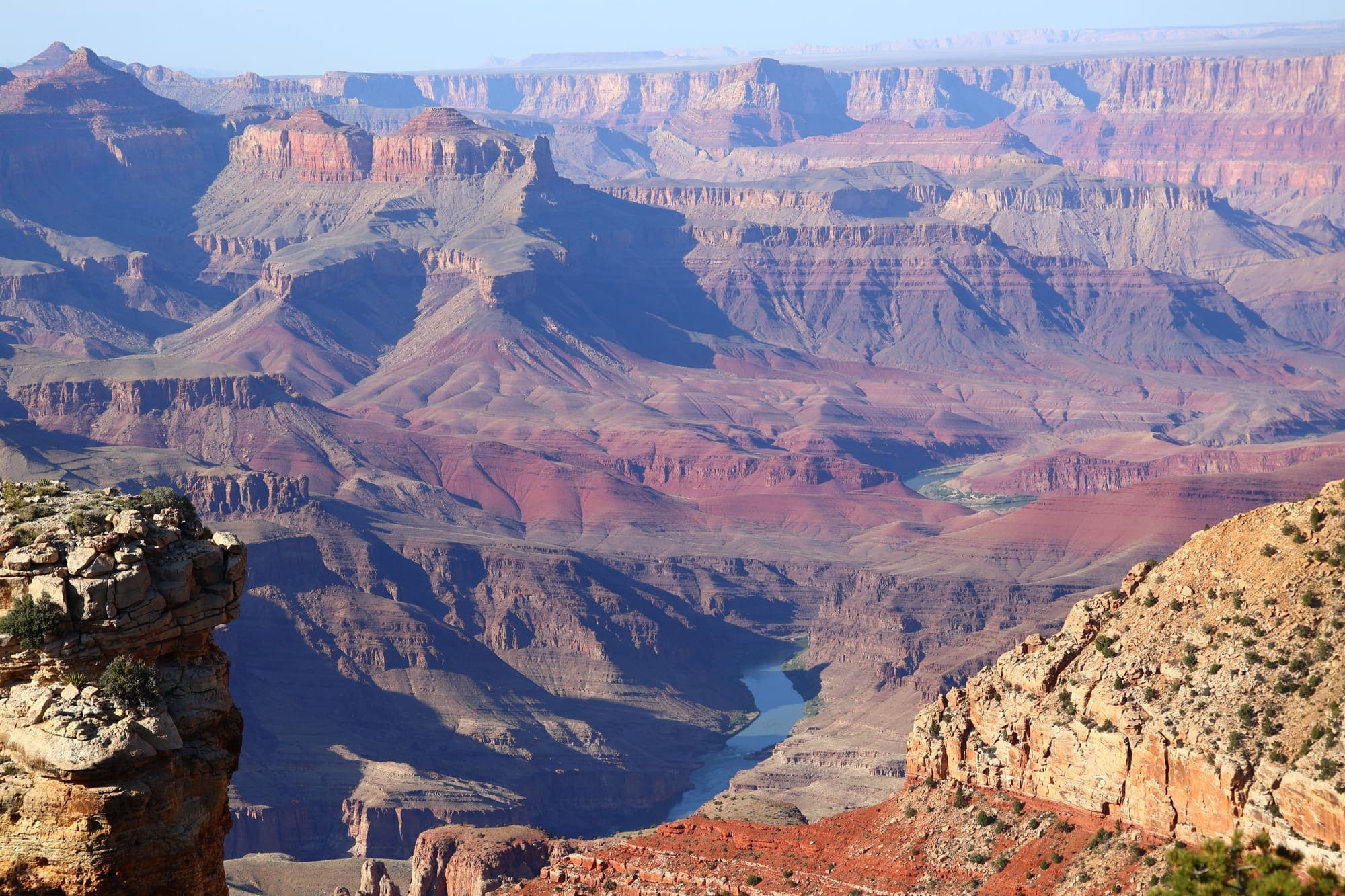 O Grand Canyon visto da borda, com paredões em camadas avermelhadas e o Rio Colorado correndo lá no fundo.