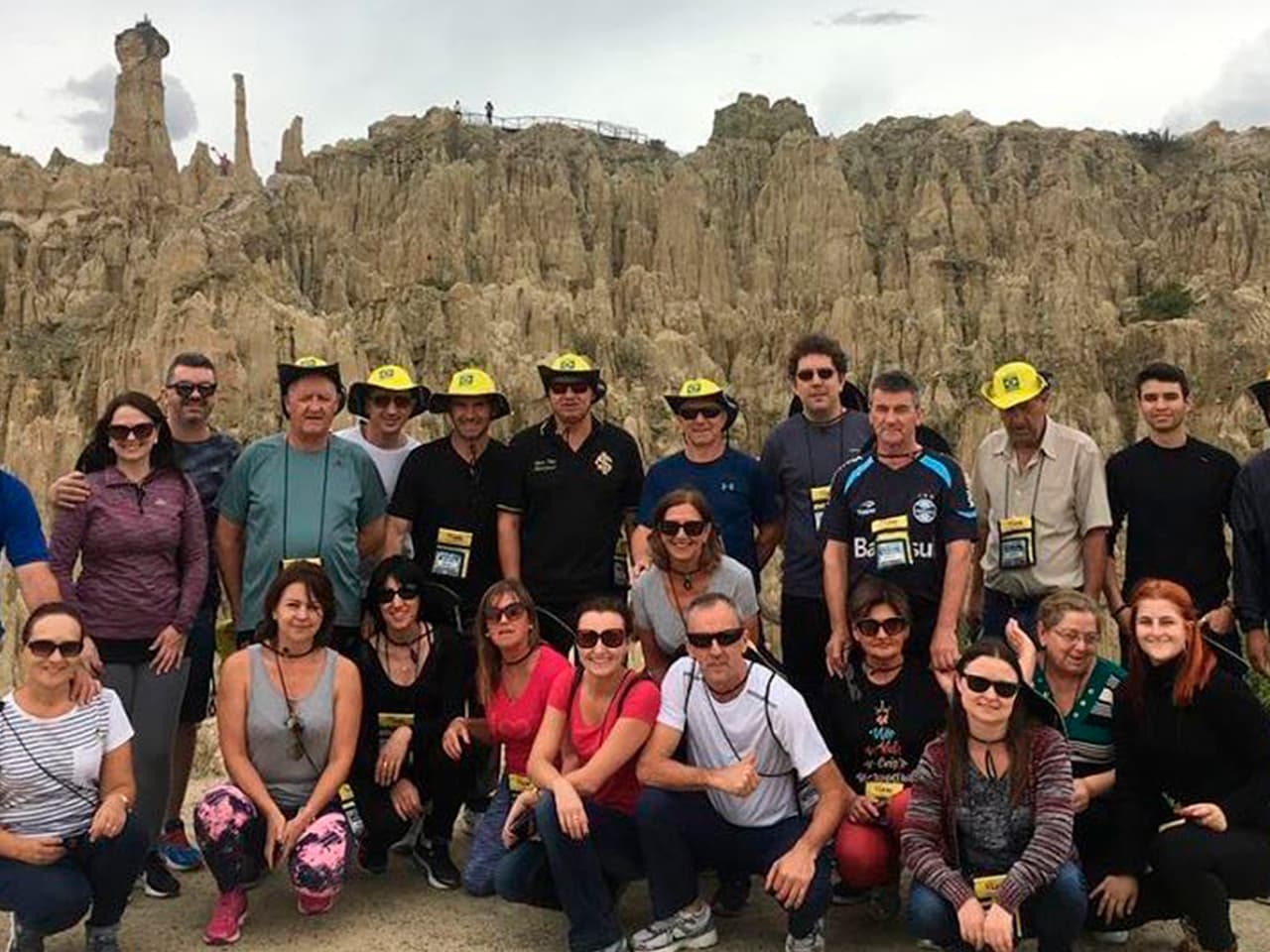Grupo da Leão Viagens com chapéus amarelos diante de um vale de formações rochosas pontiagudas.