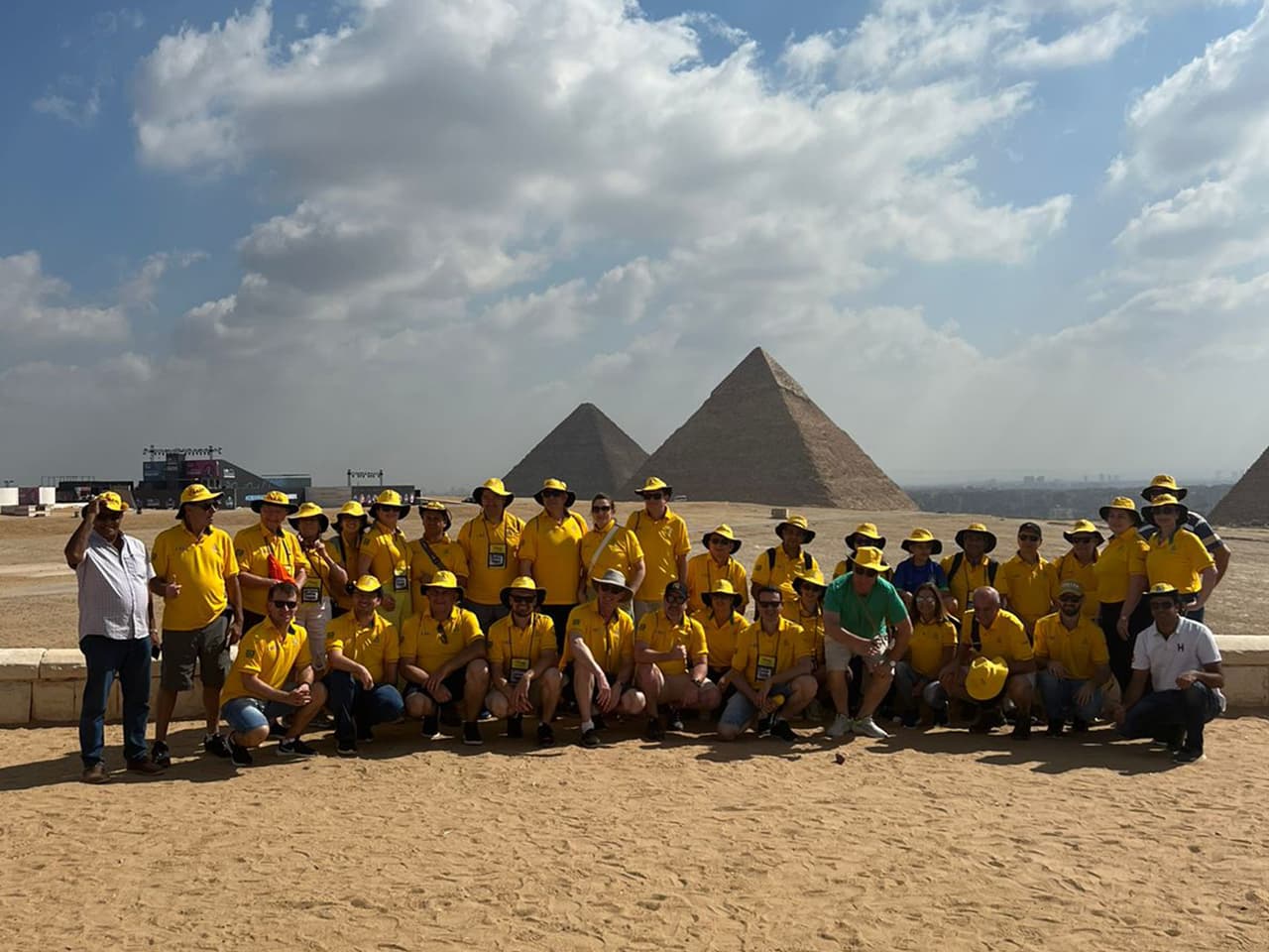 Grupo Adama, de camisas e chapéus amarelos, diante das pirâmides de Gizé, no Egito.